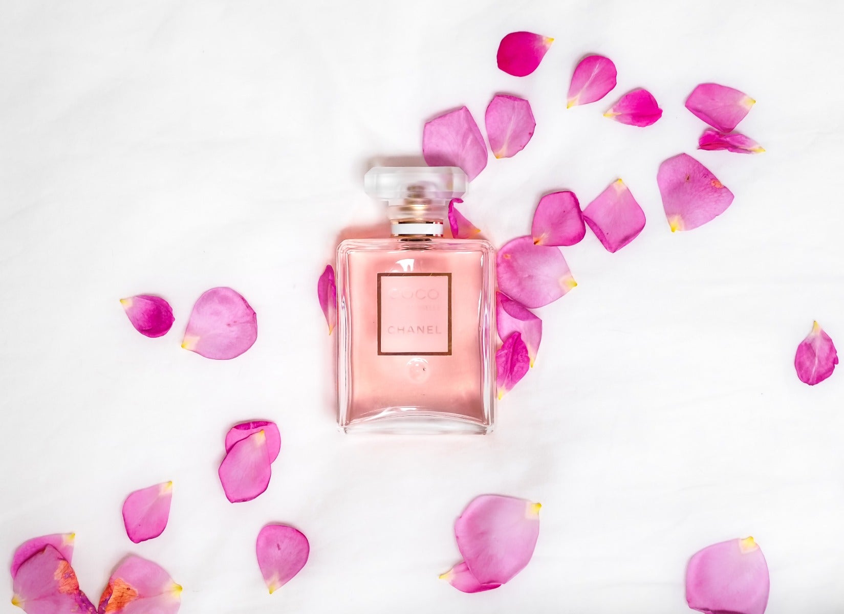 pink perfume in clear glass chanel bottle on marble table with pink flower petals surrounding