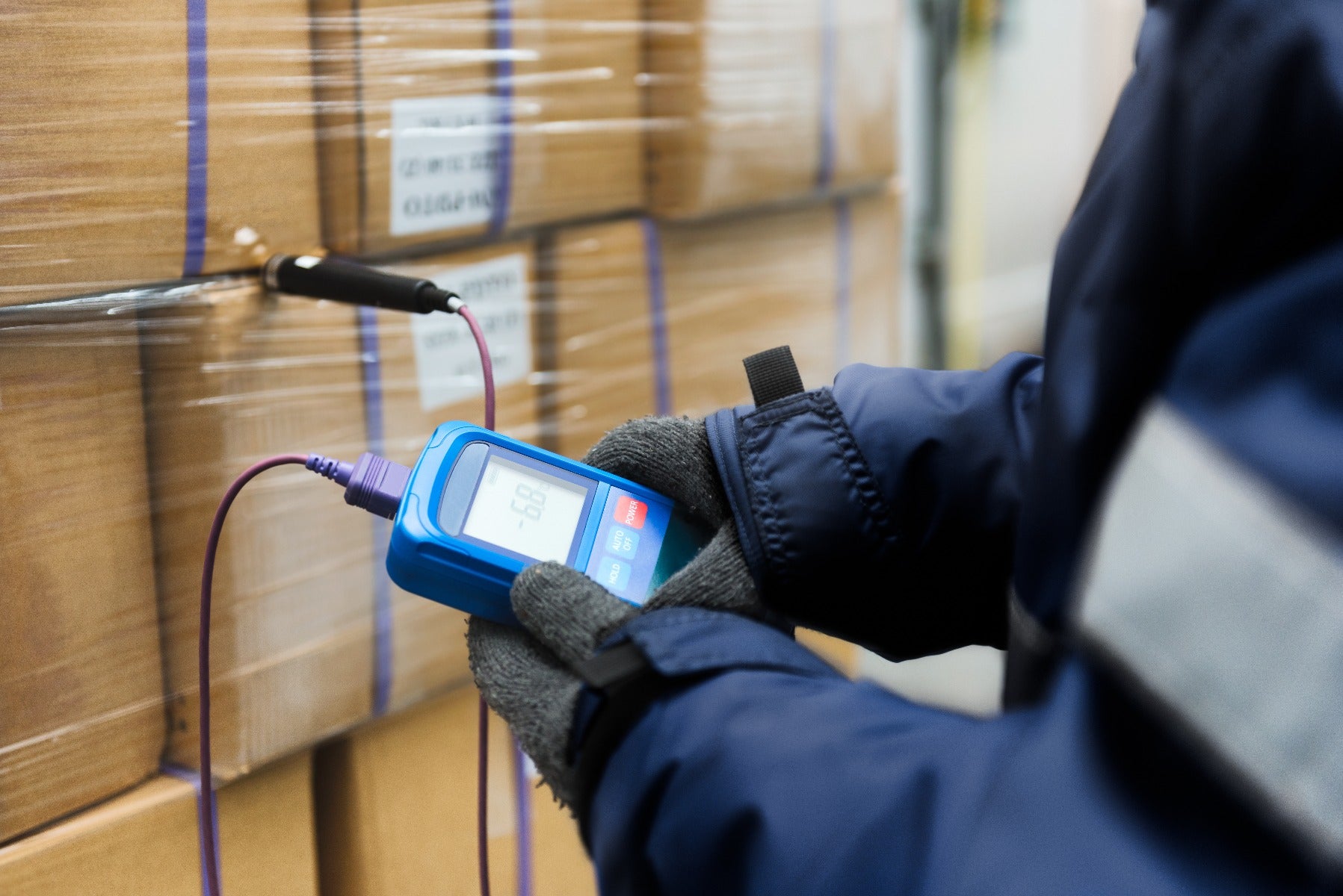 person wearing gloves checks temperature of corrugated boxes wrapped in stretch film in warehouse