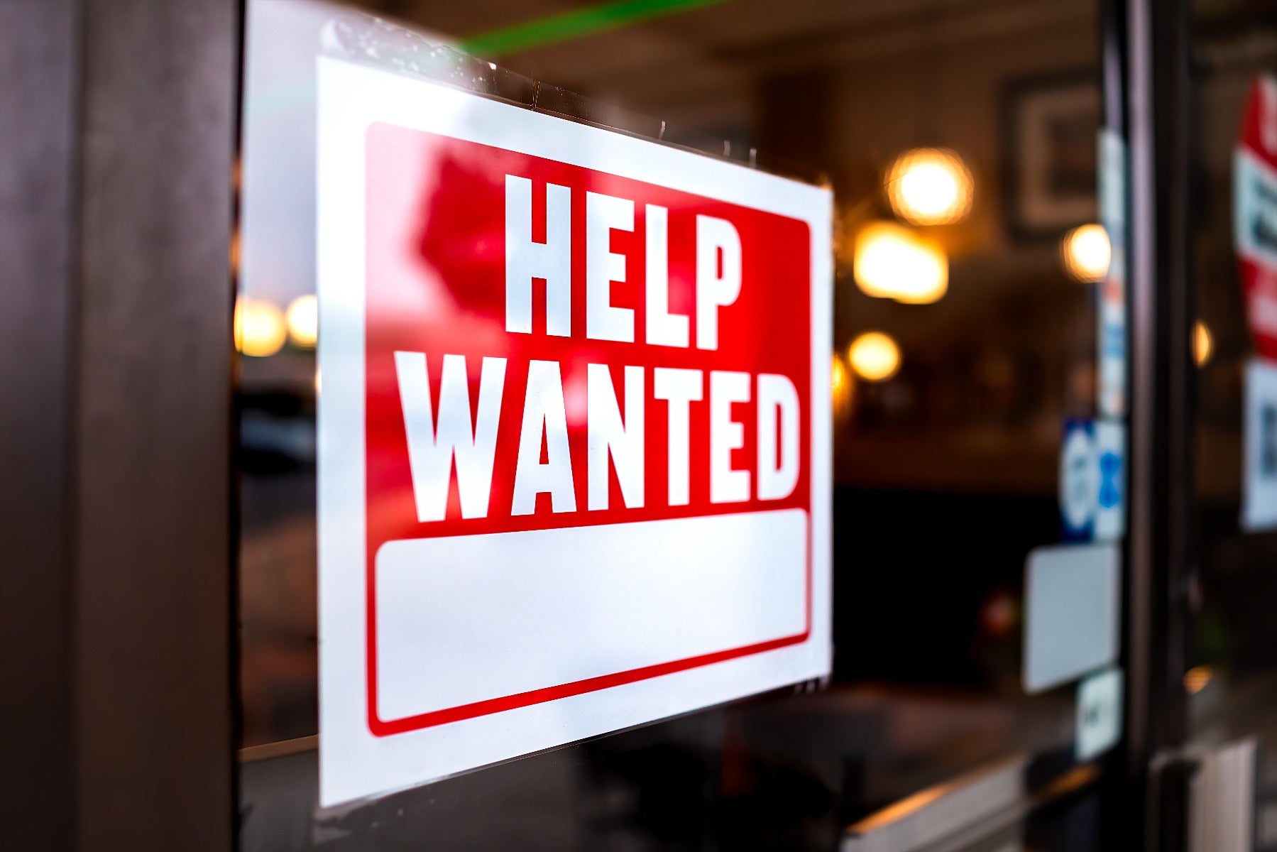 red and white help wanted sign in storefront window