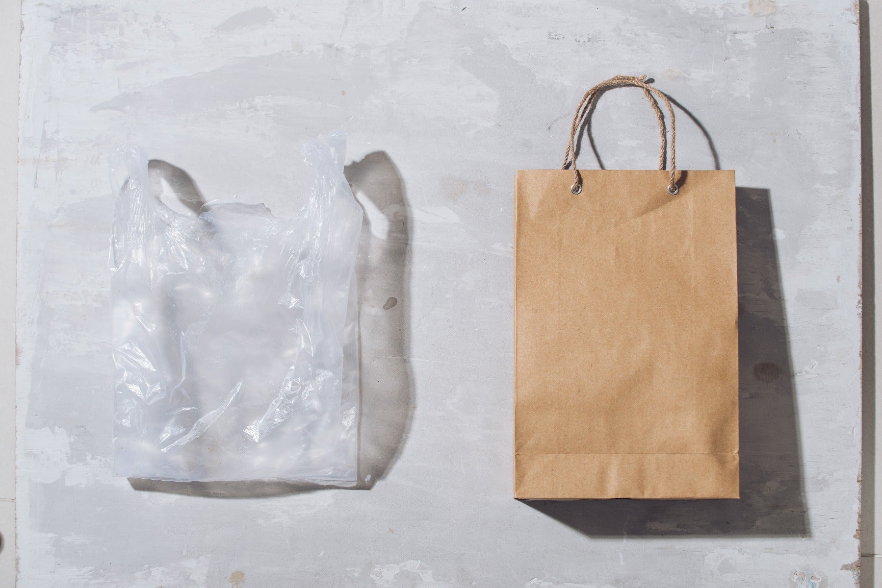 clear plastic bag and brown paper bag side by side on grey background