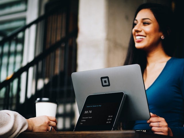 smiling woman sells coffee across shop counter