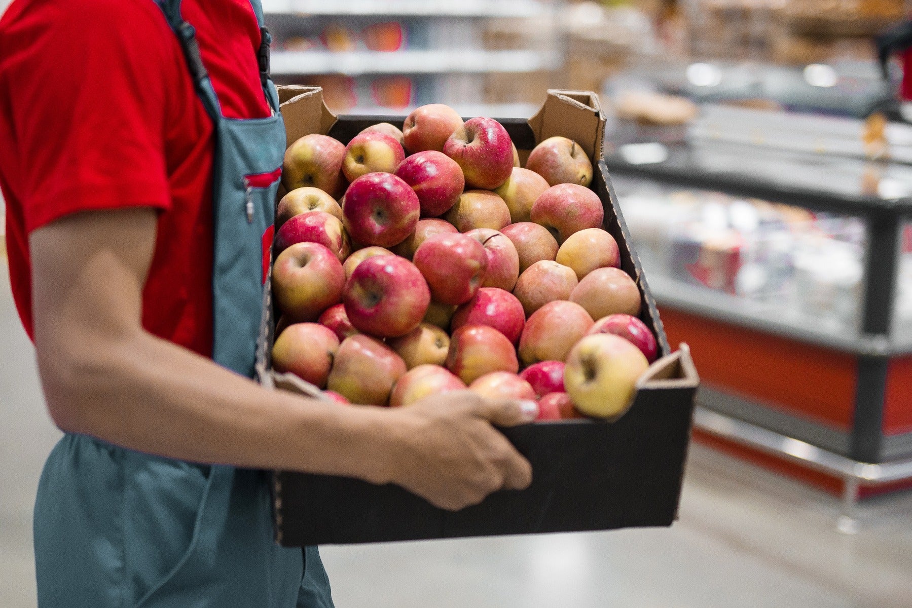 grocery employee carrying open retail ready corrugated box full of red apples